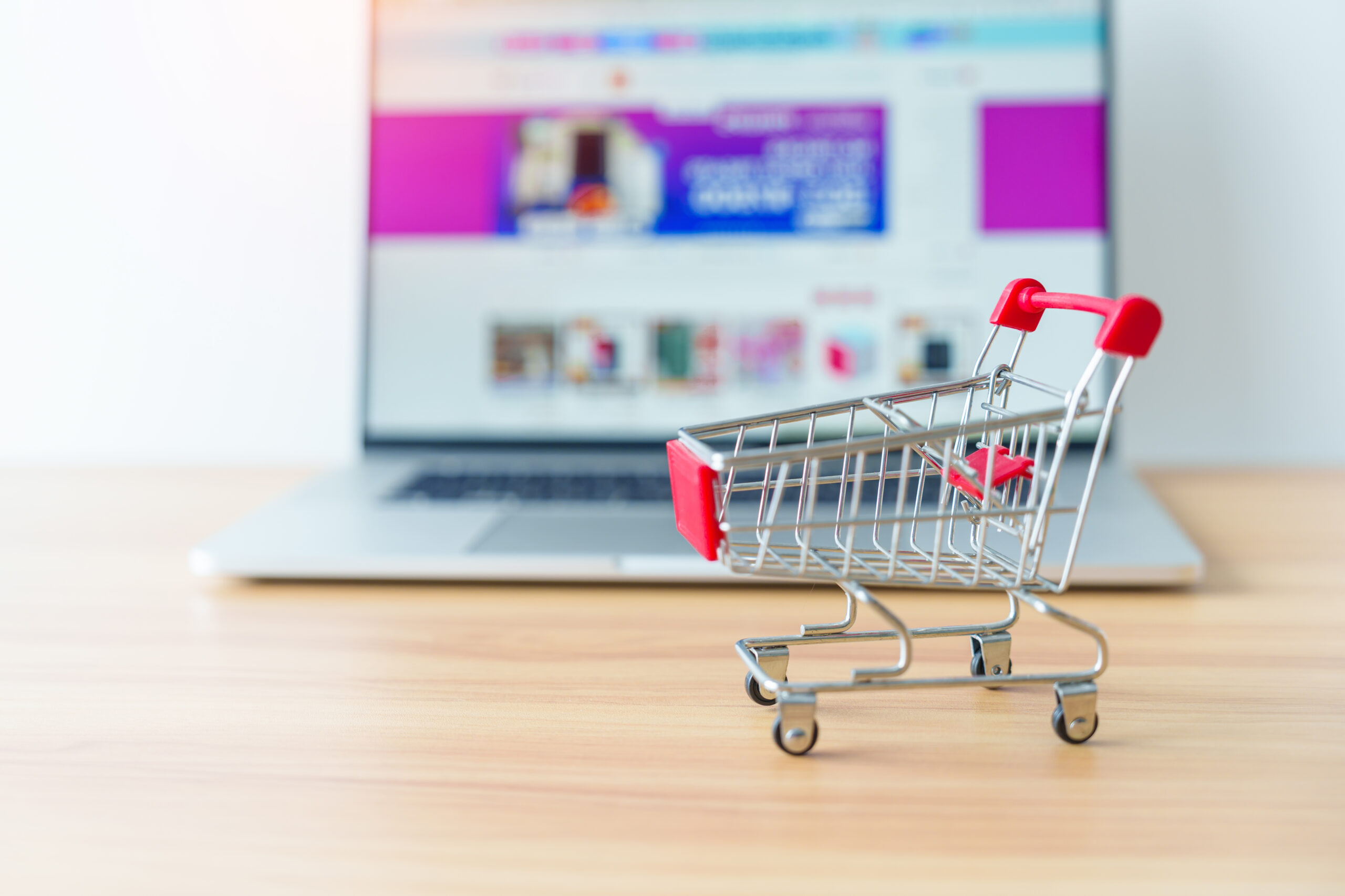 Chariot de courses miniature devant un écran d'ordinaeur ouvert sur un site e-commerce pour illustrer le concept de la localisation de site e-commerce
