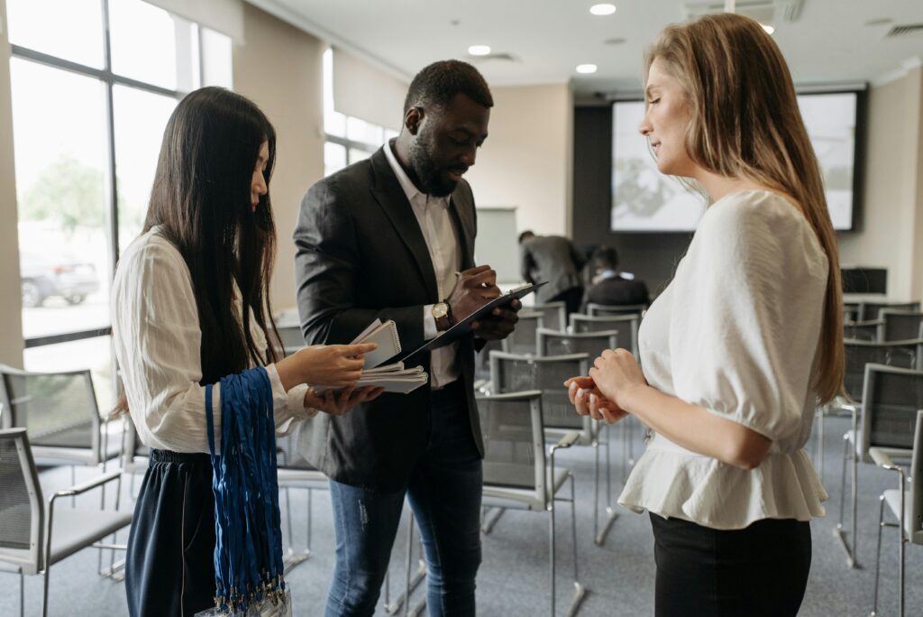 Deux femmes et un homme debout dans un bureau, discutant business.