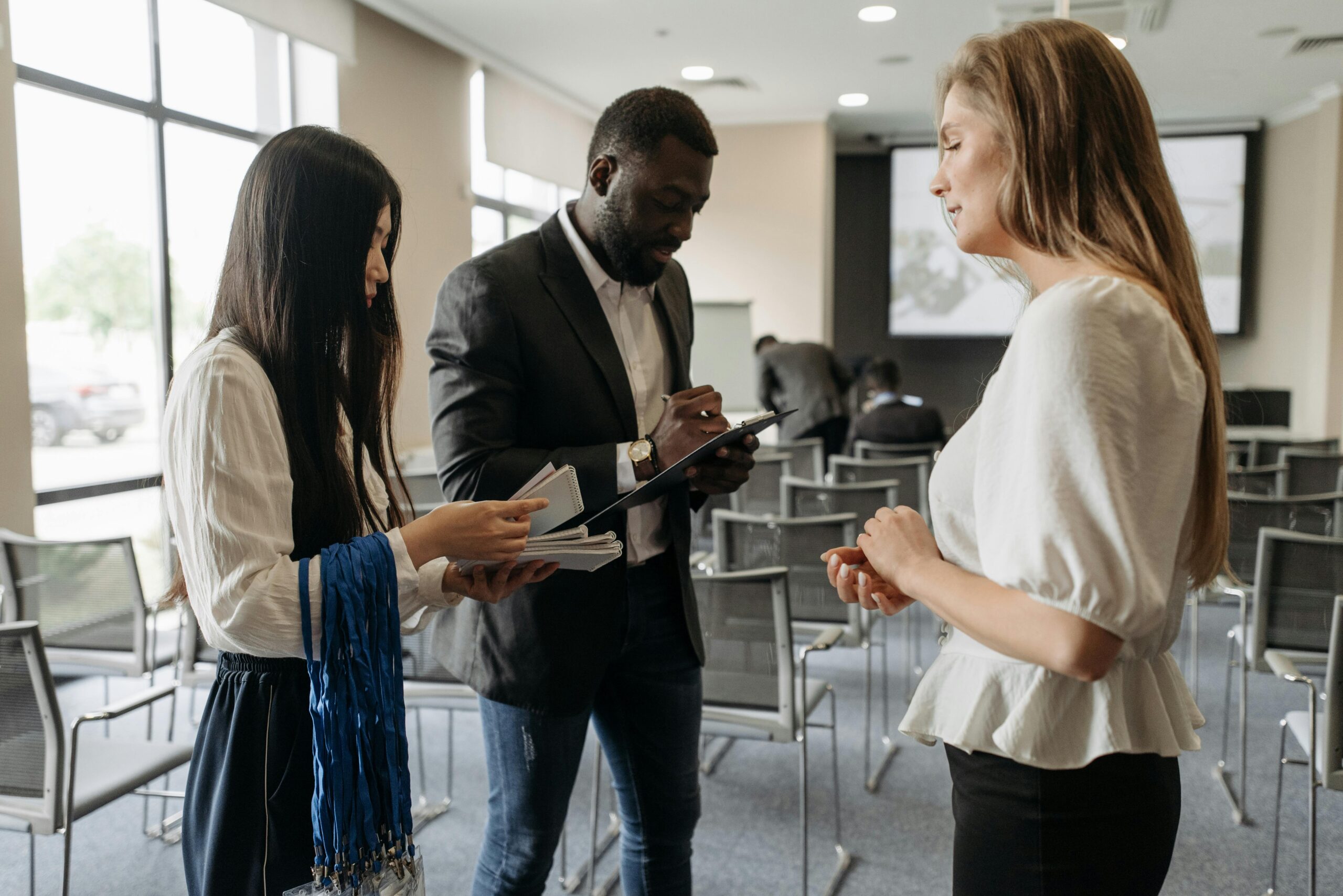 Deux femmes et un homme debout dans un bureau, discutant business.