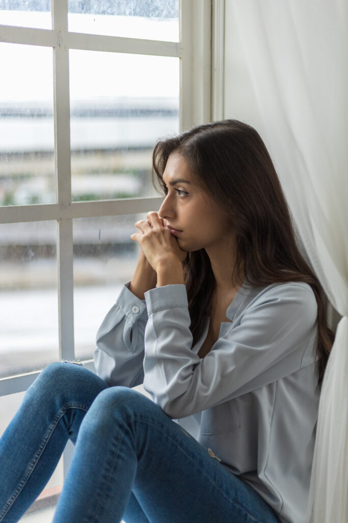 Jeune femme assise au bord d'une fenêtre, l'air triste et regardant au loin