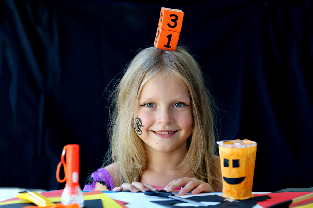 Une petite fille tient sur sa tête un calendrier en bois avec la date du 31 octobre.