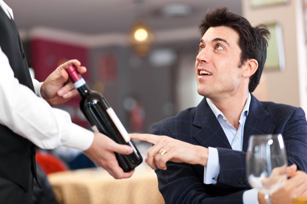 Homme jeune demande des précisions au sommelier sur la provenance d'un vin.