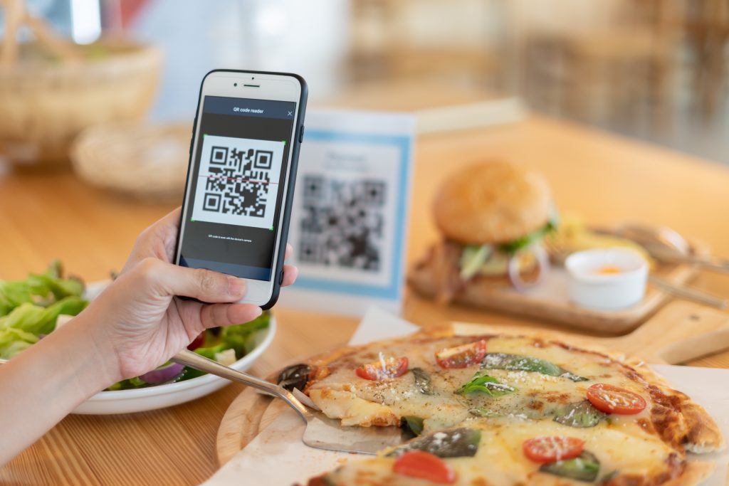 Main tenant un téléphone avec un QR code pour accéder à un menu de restaurant.