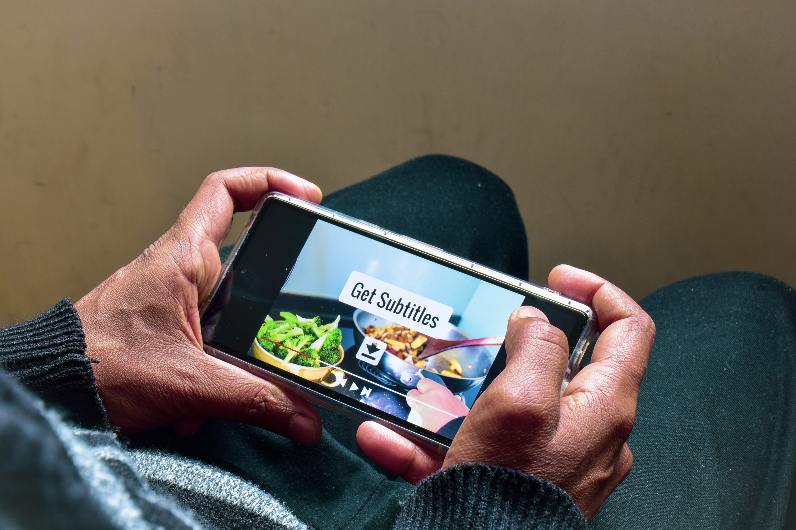Un homme regarde une vidéo de recettes de cuisine sur son smartphone avec le message Get Subtitles. Générer les sous-titres pour la traduction en langues étrangères, mise au point sélective.