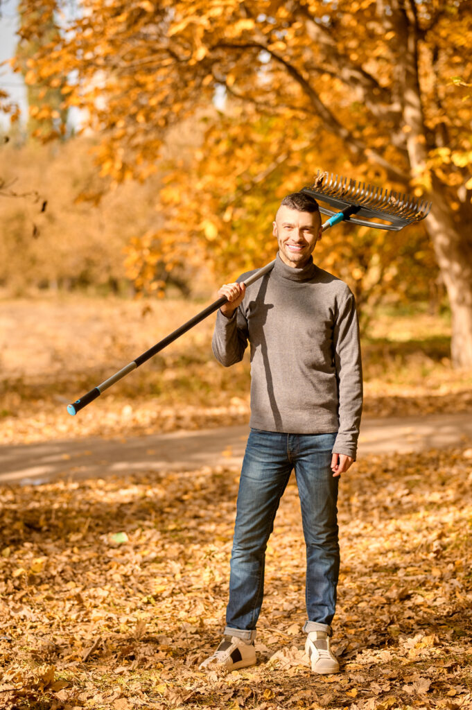 Jeune homme portant un rateau sur son épaule dans un paysage d'automne. 